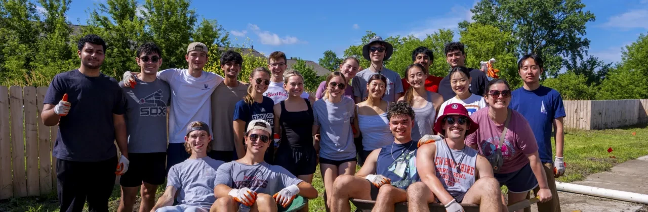 A large, diverse group of smiling young adult interns and professionals standing together outdoors during a community volunteer outing on a sunny day.