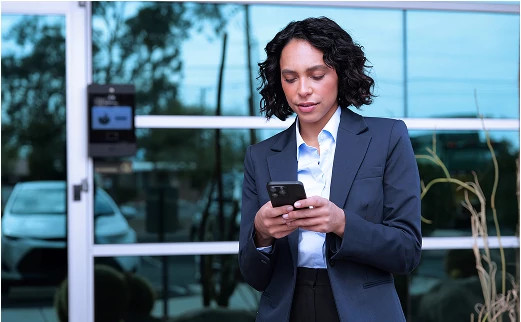 Woman holding a phone with LiftMaster access control module in the background, illustrating secure mobile entry for small business owners